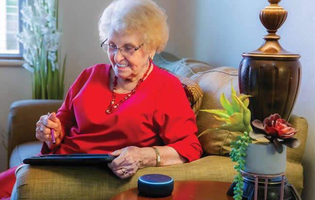 A smiling woman sitting on her couch with her iPad and Alexa.